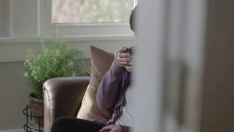 Medium tracking shot of a lady drinking coffee while watching television Stock Footage 70809621