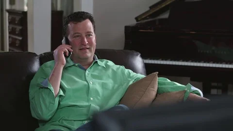 Medium tracking shot of man talking on the phone in his living room Stock Footage 71343556