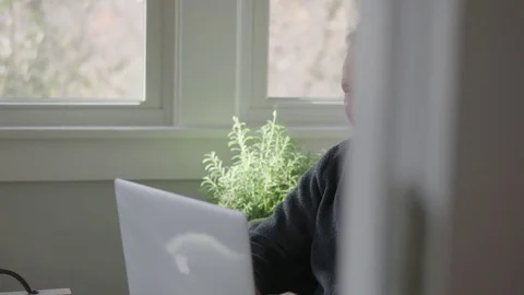 Medium tracking shot of older man working on a laptop in sunroom Stock Footage 70809787