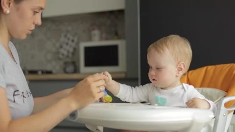 Medium view. Mom feeds a small child with a spoon. A little boy sits in a Stock Footage 133440081