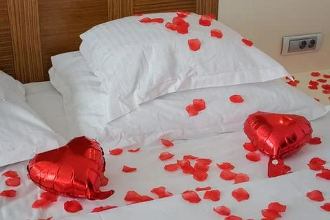 Medium View of Romantic Bed with Pillows, Rose Petals and Heart Balloons Foto stock
