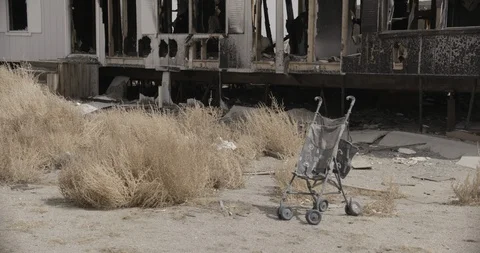 Medium Wide Shot of Stroller in Yard of Burnt out Desert Home Stock Footage 89942231