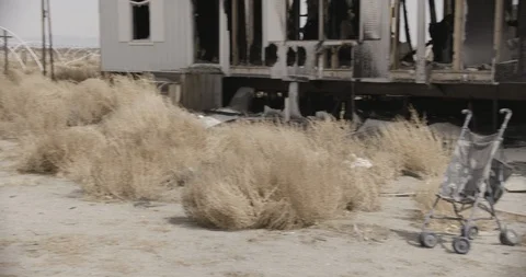 Medium Wide Shot of Stroller in Yard of Burnt out Desert Home - Pan Stock Footage 89942238