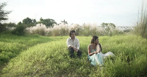 Medium wide shot of a young Asian couple sitting together in a lush green Stock Footage 346819352