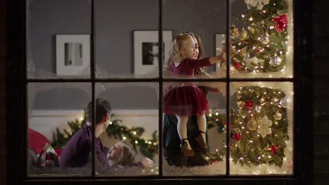 Medium zoom in shot of family decorating Christmas tree behind window / Cedar Stock Footage