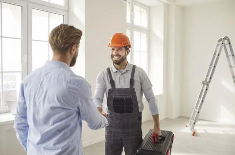 Meeting shaking hands in empty room near ladder, two men interacting, worker Stock Photos