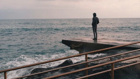 Melancholy young boy standing at pier. Lonely boy looking at rainy stormy sea. Stock Footage 114016164