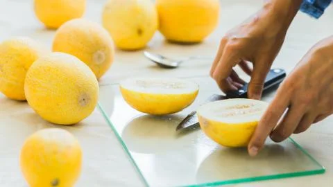 Melon berries on the kitchen table, hands cut melon into halves . Stock Photos