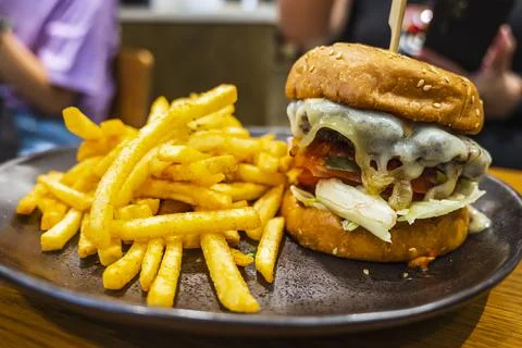 Melted cheese oozing down a hot hamburger with french fries Stock Photos