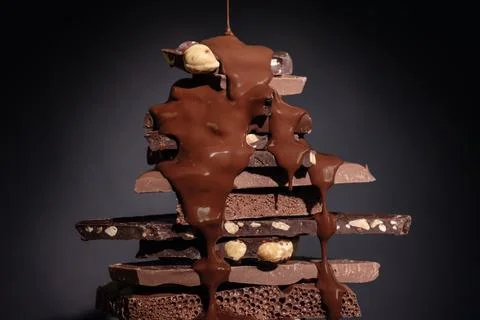 Melted chocolate pouring into a stack of chocolate pieces on dark background. Stock Photos