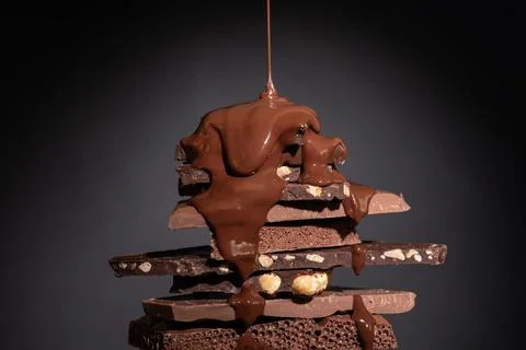 Melted chocolate pouring into a stack of chocolate pieces on dark background. Stock Photos