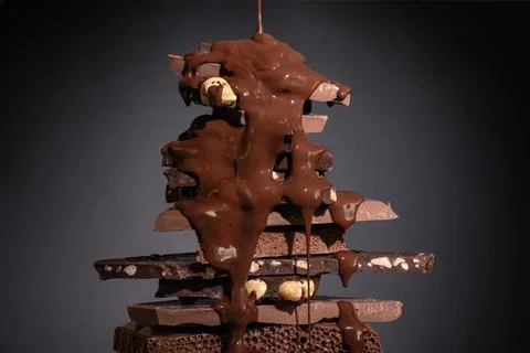 Melted chocolate pouring into a stack of chocolate pieces on dark background. Stock Photos