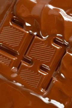 Melted chocolate stream flowing across grooved chocolate bar close up 库存照片