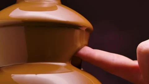 Melted milk chocolate flows in a chocolate fountain. A man dips his finger in Stock Footage 148355693