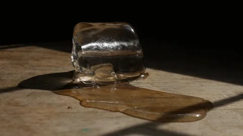 Melting ice cube with water puddle on rustic wooden table Vidéo 337042291