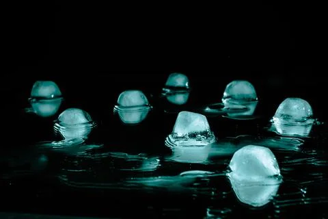 Melting ice cubes are reflected in a mirror surface against a dark background Stock Photos