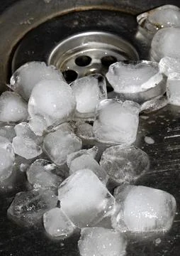 Melting ice cubes dripping down a sink plug drain silver metal basin Stock Photos