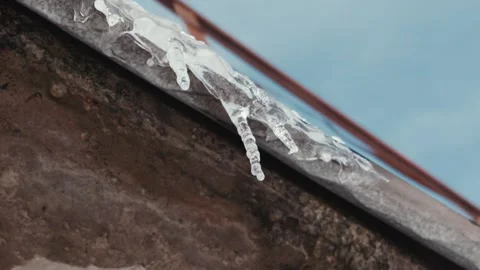 Melting icicles dripping water from rusty roof gutter during spring thaw Stock Footage 329908504