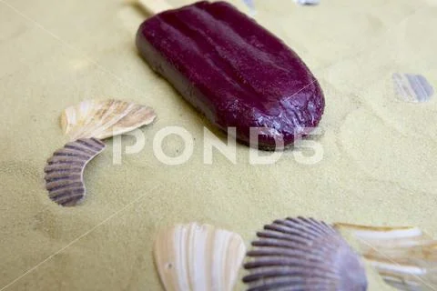 Melting popsicle on sand with shells Stock Photos
