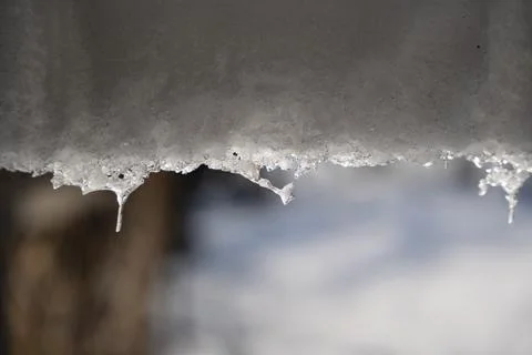 Melting snow at the edge of a rooftop, with icicles and droplets of water Stock Photos