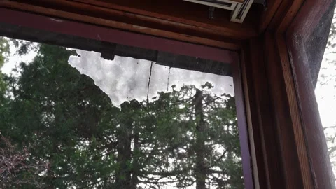 Melting snow hangs from a rooftop viewed through a window Stock Footage 329546099