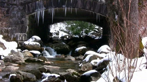 Melting spring snow around a small mountain stream flowing under bridge with sou Stock Footage 363313