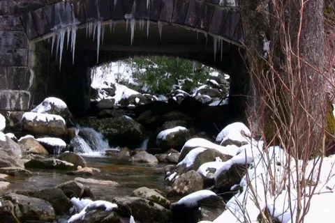 Melting spring snow around a small mountain stream flowing under bridge Stock Footage 365676