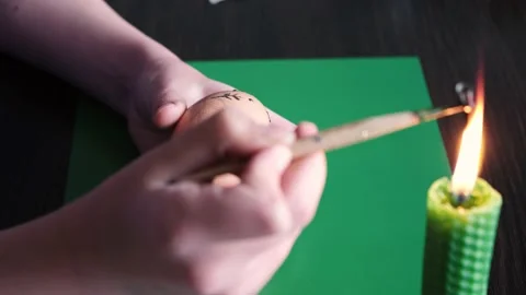Melting the wax over the candle, with the help of a pen, the girl puts a pattern Stock Footage 234708960