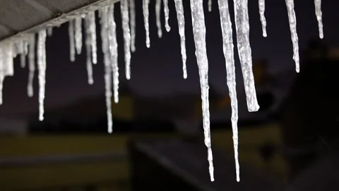 Melting winter icicles dripping from a dark roof edge at night Stock Footage 341433679
