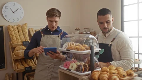 Men in bakery reviewing tablet surrounded by pastries and bread in indoor s.. Stock Footage 297594752