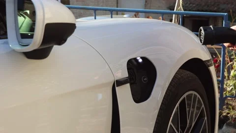 Men in black jacket charges a white electric car on the street from charging Stock Footage 233604058