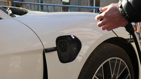 Men in black jacket charges a white electric car on the street from charging Stock Footage 233604578