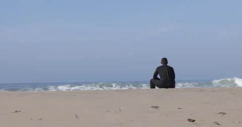 A men in a black wet suit is staring at the white powerful waves to meditate Stock Footage 244807676