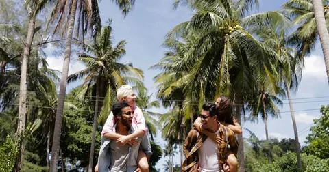 Men Carry Woman On Back, Two Cheerful Couples Running Outdoors Through Palm Stock Footage