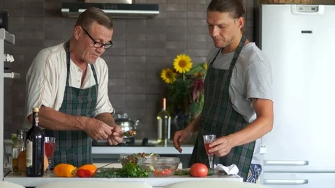 Men cook dinner together. An elderly pensioner and a young man tasting a Stock Footage 96456635