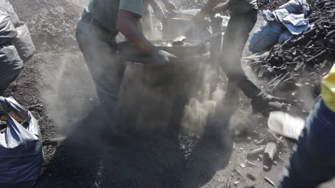 Men in dirty clothes sifting through burnt logs firewood packing coal into sacks Stock Footage 142513895
