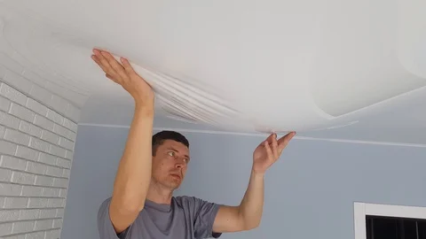 Men is drain water from a stretch ceiling filled with water through a tube. Stock Footage 128256862