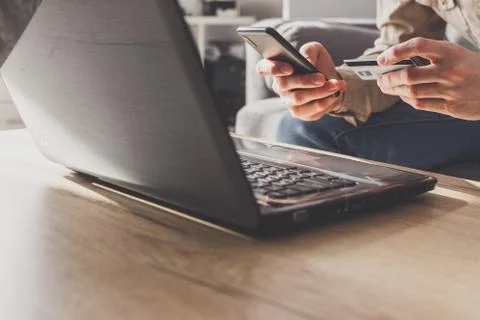Mеn entering secure code on smartphone while shopping online using laptop with Stock Photos