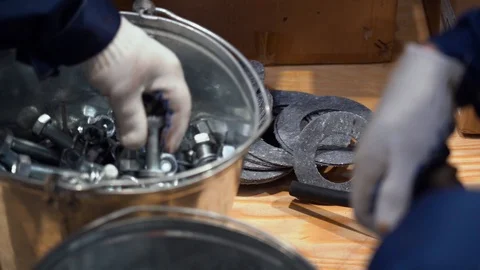 Men in gloves are picking out metal bolts with screwed nuts from steel buckets Stock Footage 126356630