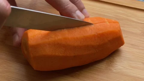 Men hands are cutting a large carrot in half on wooden cutting board in close-up Stock Footage 233621638