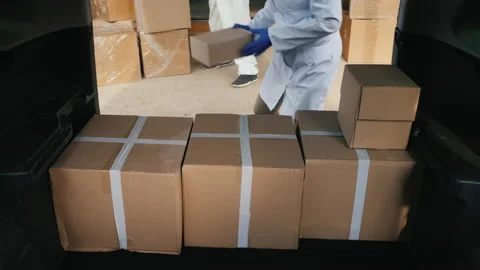 Men movers in protective suits load cardboard boxes with medicines into the car Stock Footage 141904002