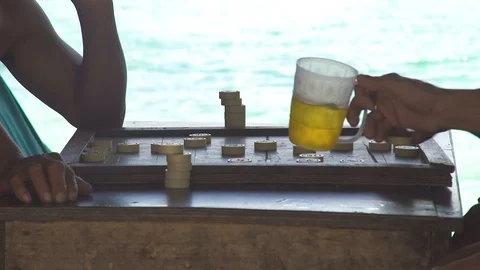 Men playing backgammon and drinking beer from mug on seashore in shadow. Men Video stock 95674255