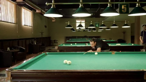 Men playing billiards, hitting balls with cue into pockets on billiard table. 4K 動画素材 109413002