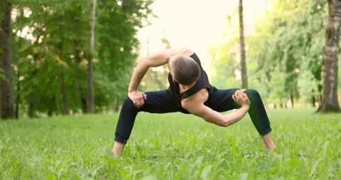 Men practicing yoga and meditating in park at sunny summer day. Young man doing Stock Footage 156524145