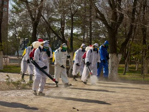 A men in a protective disinfection suits sprays sterilizer on the park square Stock Photos