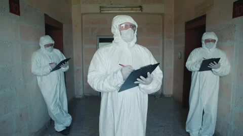 Men in protective suits and goggles hold paper folders in their hands and write Stock Footage 131376855