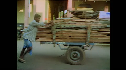 Men pushing a cart of lumber down busy street - India Stock Footage 240051615