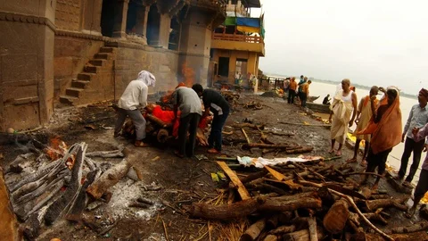 Men put wood on pyre with corpse people carry another dead body wrapped in orang Vídeos de archivo 99006924
