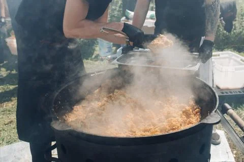 Men putting pilaf from cauldron into container. Stock-Fotos