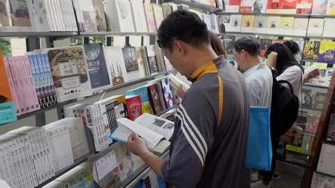 Men reading in front of bookshelf in shanghai Book Exhibition 스톡 동영상 124995693